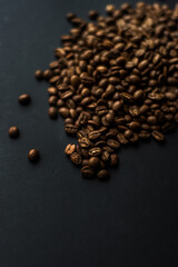 Close up of brown coffee beans in natural light on black table, black background in a dark theme. Moody picture with shadows. Sun rays.