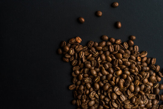 Close up of brown coffee beans in natural light on black table, black background in a dark theme. Moody picture with shadows. Sun rays.