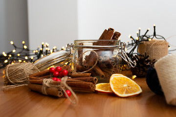 Glass jar full of cinnamon sticks with christmas lights in the background, festive ornaments, diy handmade decorations, wooden table rustic style, winter mood