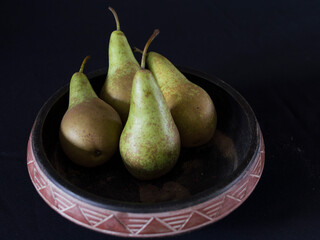 four pears in a bowl with black background