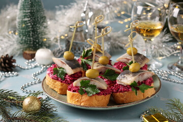 Canapes with salted herring, olives and beets on white bread croutons in a plate on a light blue...