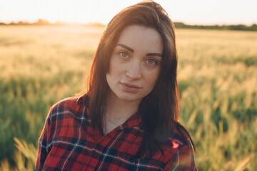 portrait of young female looking at camera in wheat field during sunset