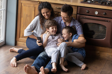 Kidding, giggling, having fun. Happy cute family of four cuddle on warm heated floor at kitchen....