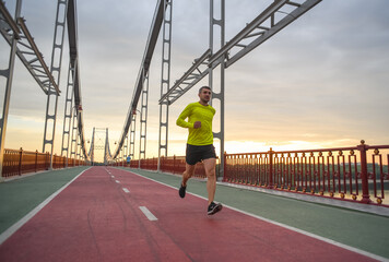 sporty man running outdoors on the bridge during sunrise