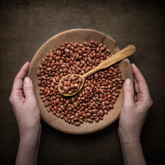Female hands holding wooden bowl of brown dried beans. Food background.