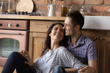 New home. Happy young husband and wife celebrate moving relocating to modern rented purchased family flat house apartment. Smiling millennial spouses hugging sitting on floor at comfy kitchen interior