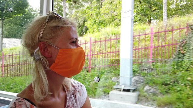 woman with surgical mask for Covid-19 pandemic in train of Rigi Mountain railways. window scenic landscape between Alps, valleys of Rigi Mountain railways and blue cog train.