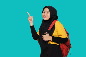Portrait of teenager muslim female student in hijab pointing at copy space