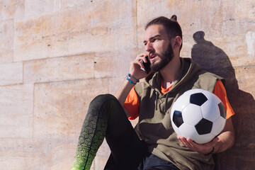 sportsman talking by phone resting with his ball