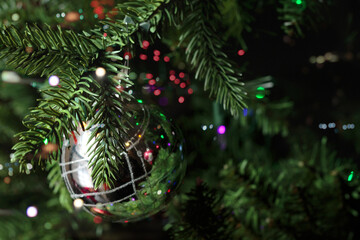 shimmering silver christmas tee ornament hanging from a christmas tree surrounded by multi-colored bokeh lights