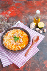 Vertical view of delicious chicken soup with noodles greens and spoon on pink stripped towel oil bottle garlic lemon on dark background
