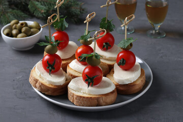 Canapes of mozzarella, cherry tomatoes, green olives, parsley on croutons of white bread on dark gray background. Festive New Year snack.