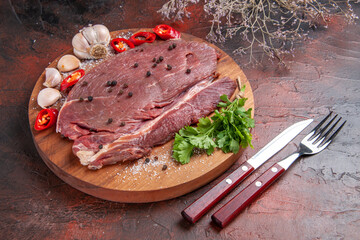 Close up view of red meat on wooden tray and garlic green lemon pepper onion fork and knife on dark background