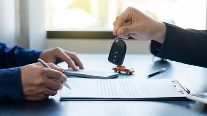 Hand holding car keys and car rental concept A close-up view of the agent, giving the customer the car keys after signing the lease, rental form and car name.