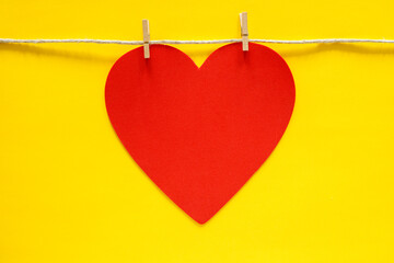 Red heart hanging on rope with small clothes pins on yellow background.
