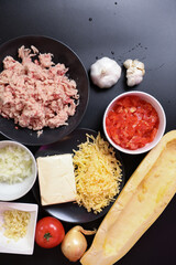A set of fresh vegetables on a wooden kitchen table for cooking. Onions, garlic, red tomato, yellow zucchini , fresh meat and cheese on the kitchen table.