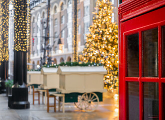 Fototapeta na wymiar Traditional red telephone booth in London and Christmas tree decorated on the blurry background
