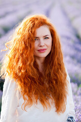 Summer portrait of a beautiful girl with long curly red hair. European girl in lavender field. Wavy Red Hair
