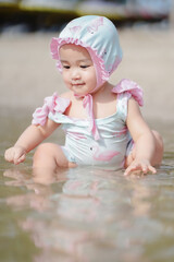 Asian cute baby girl in swimwear sitting on the sand beach on sunny day