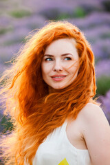 Summer portrait of a beautiful girl with long curly red hair. European girl in lavender field. Wavy Red Hair