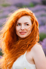 Naklejka premium Summer portrait of a beautiful girl with long curly red hair. European girl in lavender field. Wavy Red Hair