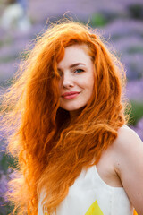 Summer portrait of a beautiful girl with long curly red hair. European girl in lavender field. Wavy Red Hair