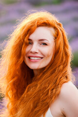 Summer portrait of a beautiful girl with long curly red hair. European girl in lavender field. Wavy Red Hair