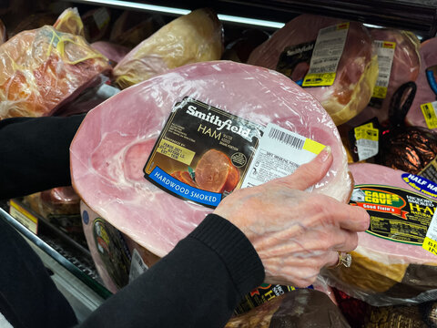 SARASOTA, FLORIDA - DECEMBER 18  2020 : Female grocery shopper selecting a Smithfield smoked ham from a refrigerated grocery store display case.