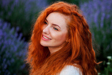 Summer portrait of a beautiful girl with long curly red hair. European girl in lavender field. Wavy Red Hair