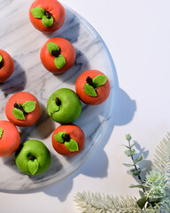Marzipan sponge apples, green and red. Tasty dessert, real favorite in Autumn and Winter. Flat lay on marble board with winter evergreens.