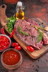 Above view of red meat on wooden cutting board and garlic green chopped pepper fallen oil bottle on dark background