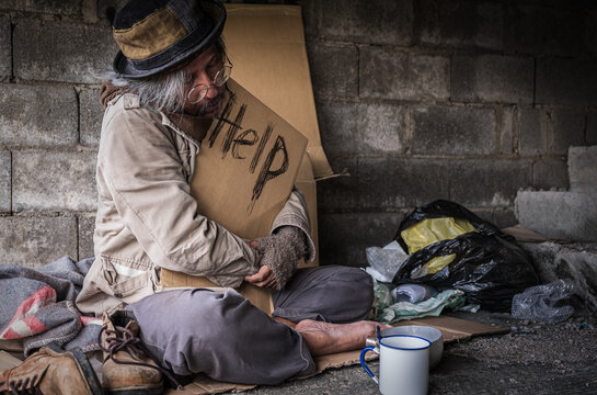 Homeless senior man with gray beard sitting and holding cardboard sign seeking help and beggar on walking street.