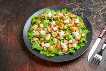 bottom view caesar salad fork and knife on oval plate on dark red background