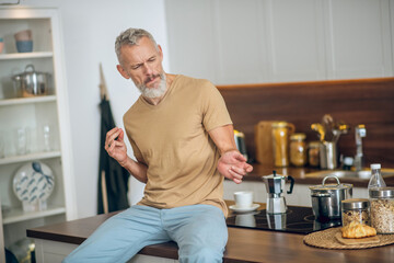 Mature man in beige tshirt in the kitchen playing air guitar