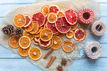 Fototapeta na wymiar cinnamon, anise, dried oranges and grapefruit slices, threads for diy projects, gift wrapping and beautiful eco Christmas decorations like wreaths arranged on a blue wooden table