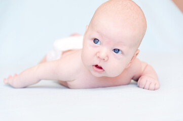 A smiling baby newborn boy with blue eyes smiles and crawls on a white sheet.
