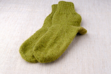 Green knitted wool socks. Warm winter clothes, made by hand. The leg garments lie on top of each other on a table covered with a light-colored cloth.