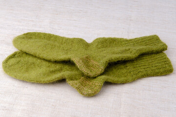 Fototapeta na wymiar Two green knitted woolen socks lie on top of each other. Handmade footwear. The table is covered with a light-colored cloth with a fine texture.