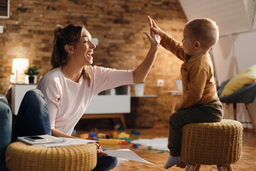 Cheerful mother giving high-five to her small son at home.