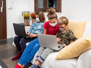 Children with masks coronavirus study in lockdown with laptop on the sofa at home, using the wi-fi...
