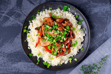 Stir fried turkey pieces with mushroom, carrot and garlic on top of couscous. Appetizing hot meal garnished with green onion served on the grey table