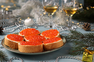 Sandwiches with red caviar on white bread croutons on a plate on light blue background. Festive snack. Horizontal format