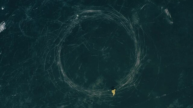 Male ice skating on frozen lake, drawing circles on ice. The drone is slowly gaining altitude.