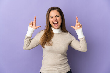 Middle age Brazilian woman isolated on purple background with fingers crossing