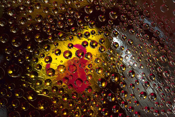 Multi colored drops of water are located on a black-yellow mirror background with a red silhouette of a bull. Abstract fantasy. 3D render.