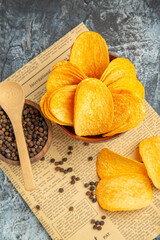 Vertical view of delicious homemade chips and pepper bowl with spoon on newspaper on gray background