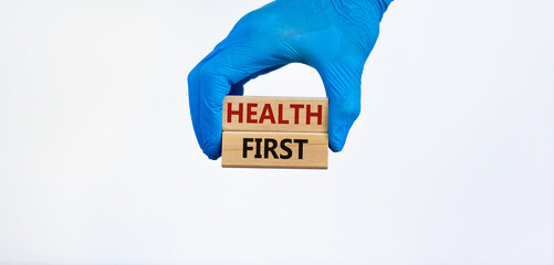 Medical and COVID-19 Pandemic Coronavirus symbol. Hand in blue glove holds wooden blocks with words 'health first'. Beautiful white background. Copy space. Medical and health first concept.