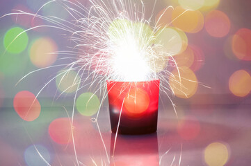 Festive Christmas bengal sparkler on blurred garland lights background