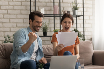 Can you believe it. Shocked millennial couple sitting on sofa screaming in delight getting official...