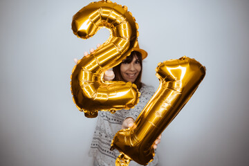 Beautiful woman celebrating the new year with comfortable clothes at home with social distancing. Celebrating 2021 with some golden balloons. 